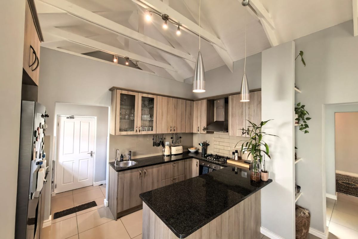 Modern kitchen featuring granite countertops, wood-finish cabinetry, gas hob with extractor, and high vaulted ceilings with exposed rafters.