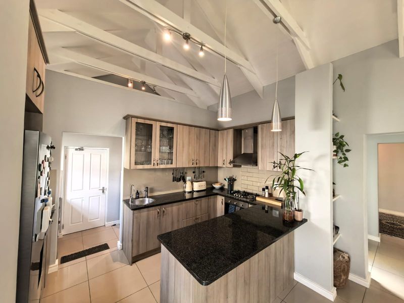 Modern kitchen featuring granite countertops, wood-finish cabinetry, gas hob with extractor, and high vaulted ceilings with exposed rafters.