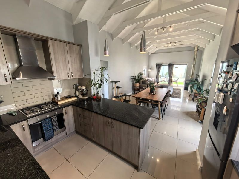 Spacious open-plan kitchen and living area featuring vaulted ceilings with exposed rafters, modern cabinetry, granite countertops, and seamless flow to the outdoor patio.