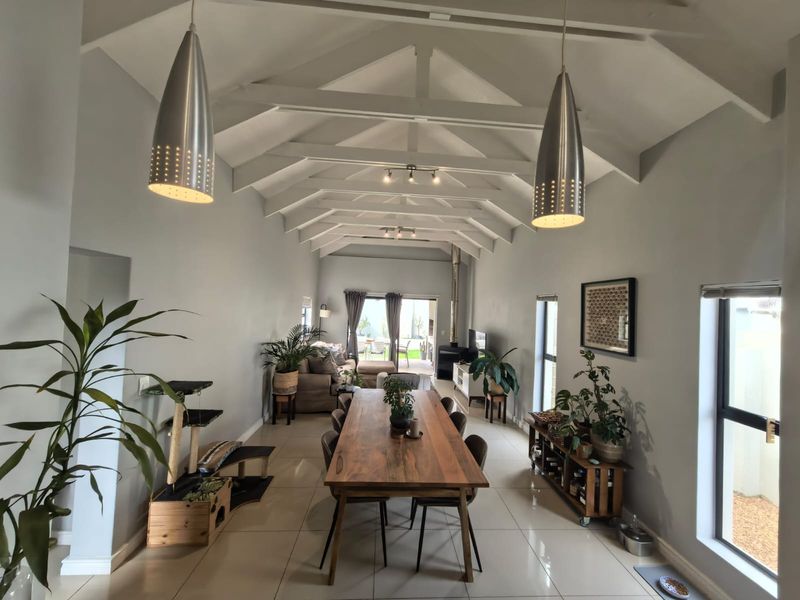 Spacious open-plan living and dining area featuring a high vaulted ceiling with exposed trusses, tiled floors, and a cozy wood-burning fireplace.