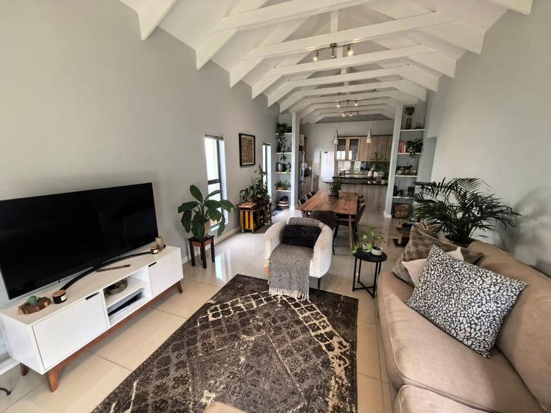 Spacious open-plan living and dining area featuring high vaulted ceilings with exposed trusses, tiled floors, and a modern integrated kitchen.