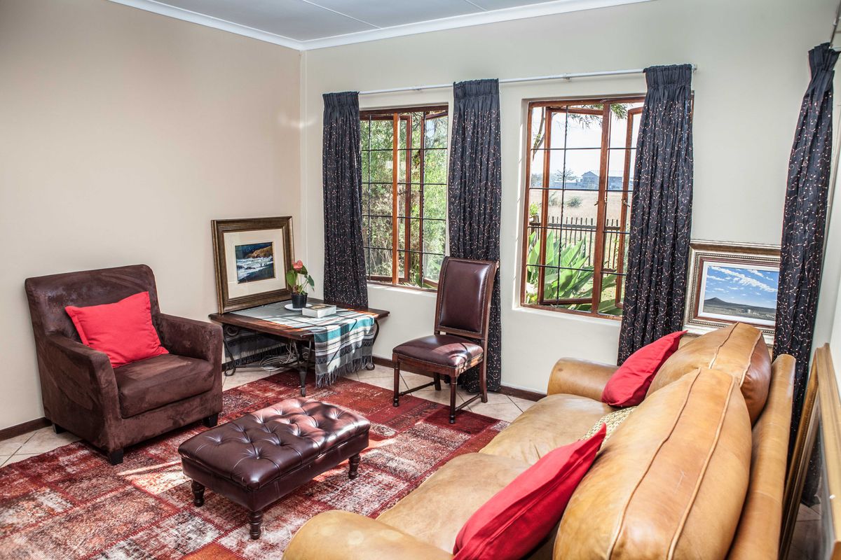 A comfortable living room featuring tiled flooring, coved ceilings, and large wooden-framed windows that provide natural light and garden views.