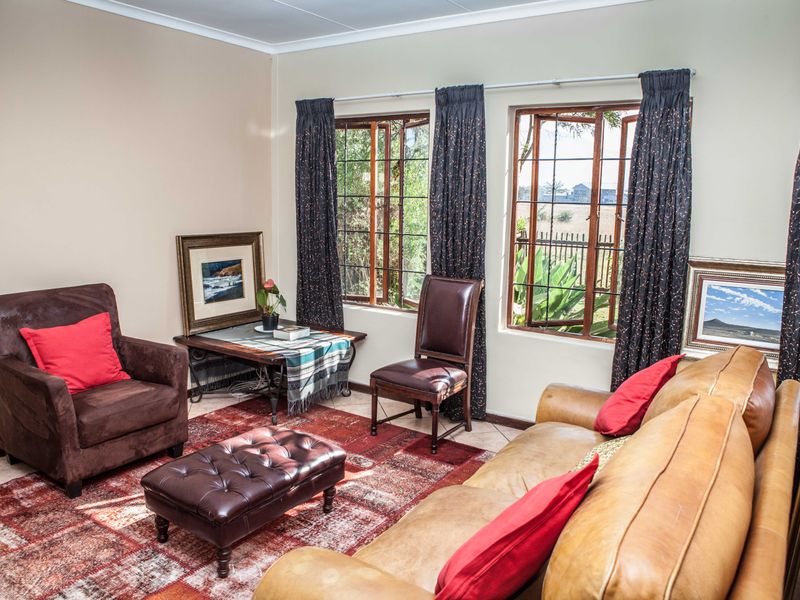 A comfortable living room featuring tiled flooring, coved ceilings, and large wooden-framed windows that provide natural light and garden views.