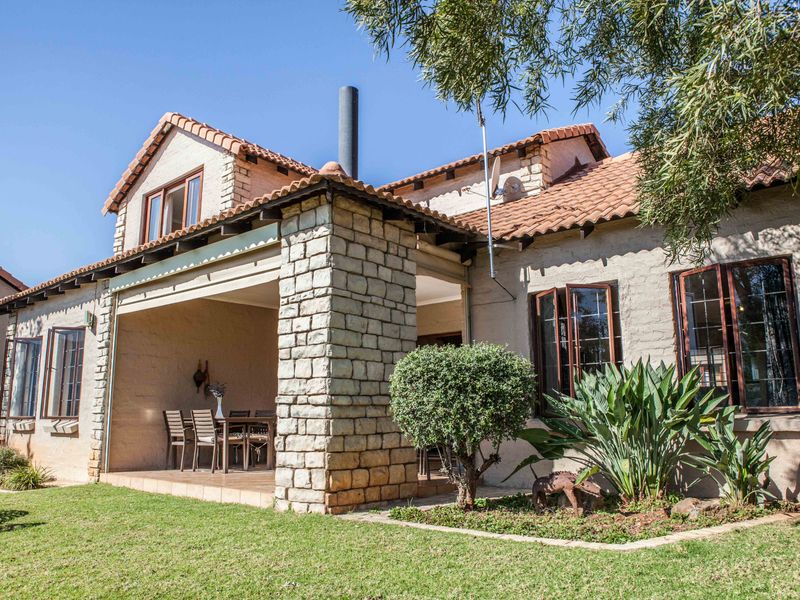 Rear view of a townhouse featuring a covered patio with stone pillar detailing, terracotta roof tiles, and established garden surroundings.