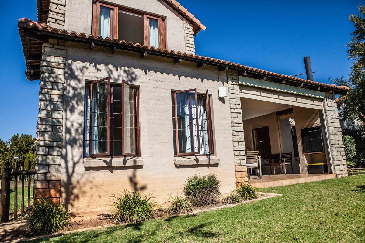 Rear view of a townhouse featuring stone cladding, terracotta roof tiles, and a covered patio area with a built-in braai.