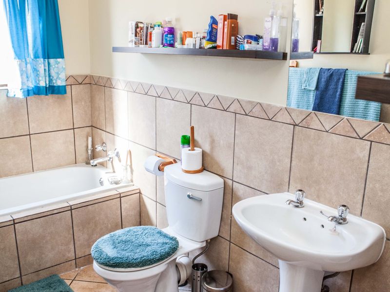 A functional bathroom featuring a bathtub, pedestal basin, and toilet with neutral wall tiling and a wall-mounted storage shelf.