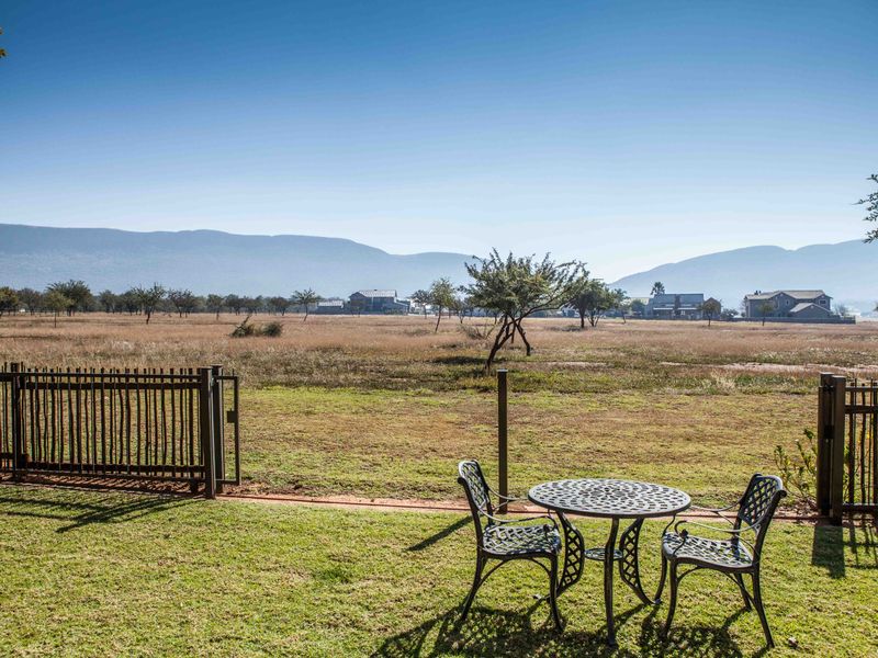 A scenic view overlooking an open field and distant mountains, featuring a manicured lawn and metal perimeter fencing.