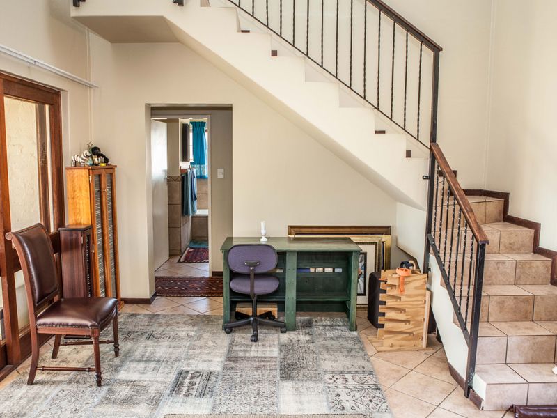 Living area featuring a tiled staircase with wrought iron balustrade, tiled flooring, and access to an adjacent room through a sliding glass door.