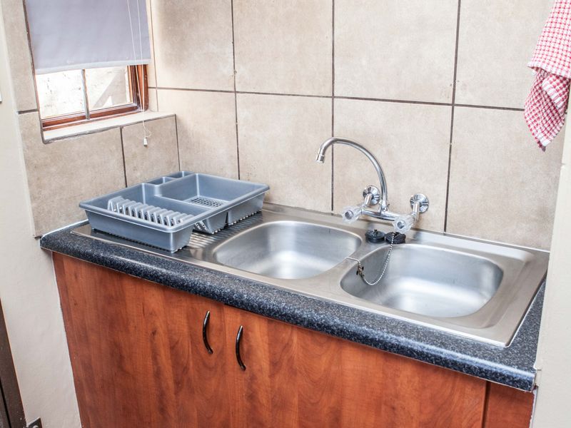 A functional scullery area featuring a double bowl stainless steel sink, laminate countertop, and wooden cabinetry with tiled splashback.