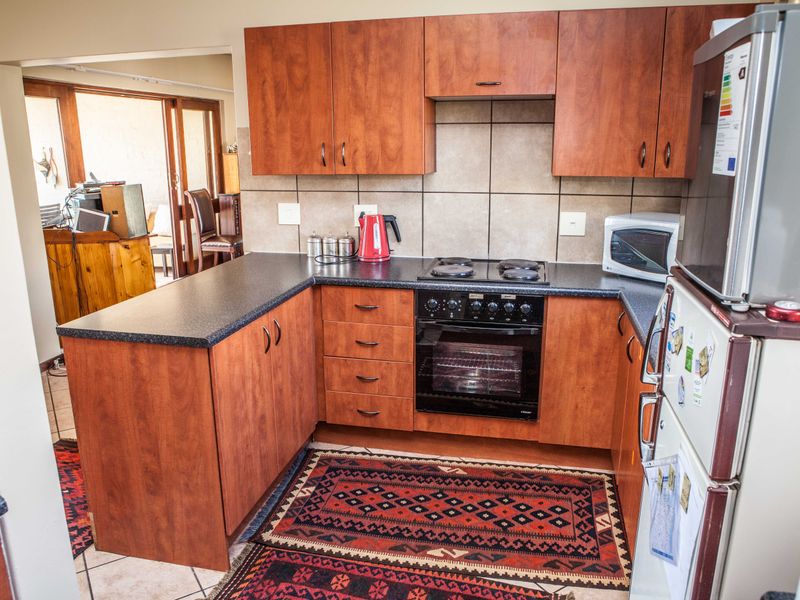 A functional kitchen featuring wood-finish cabinetry, dark laminate countertops, a built-in oven with electric hob, and tiled flooring.