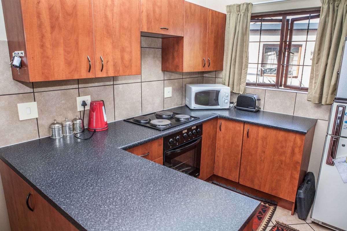 A functional kitchen featuring wood-finish cabinetry, dark laminate countertops, a built-in oven with electric hob, and tiled backsplash.