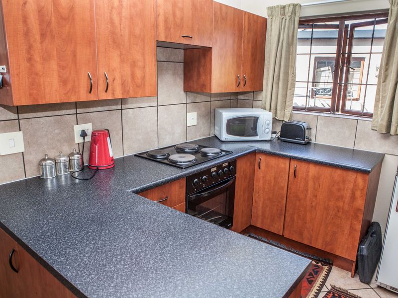 A functional kitchen featuring wood-finish cabinetry, dark laminate countertops, a built-in oven with electric hob, and tiled backsplash.