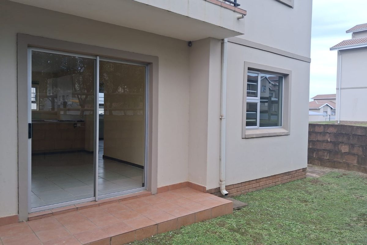 Rear exterior view of the apartment featuring a tiled patio, sliding glass door access, and a small private garden area.