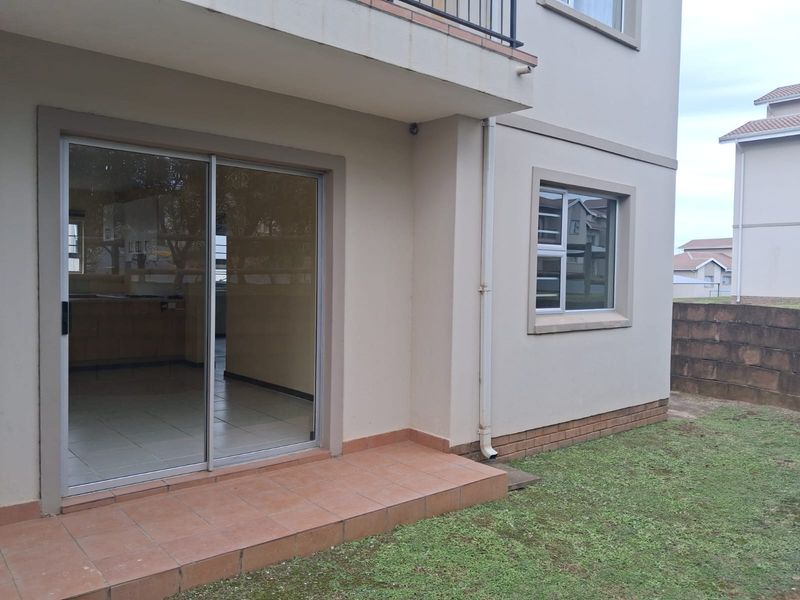 Rear exterior view of the apartment featuring a tiled patio, sliding glass door access, and a small private garden area.