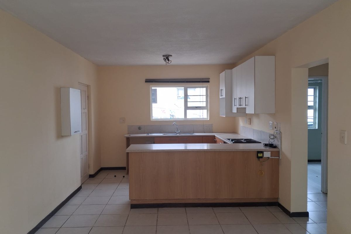 A functional, empty kitchen featuring light wood-look cabinetry, laminate countertops, a built-in hob, and tiled flooring, offering a clean canvas for updates.