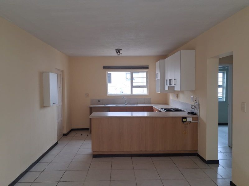 A functional, empty kitchen featuring light wood-look cabinetry, laminate countertops, a built-in hob, and tiled flooring, offering a clean canvas for updates.