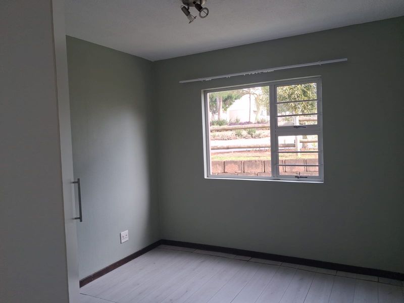 A clean, empty bedroom featuring neutral wall paint, laminate flooring, and a built-in cupboard, ready for personalization.