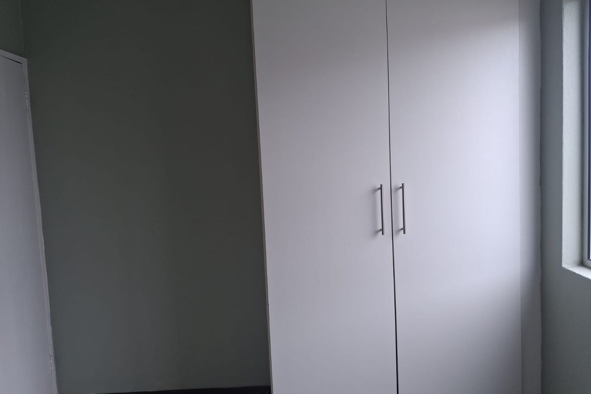 A clean, empty bedroom featuring a modern white built-in wardrobe and a window, providing a neutral space ready for personalization.