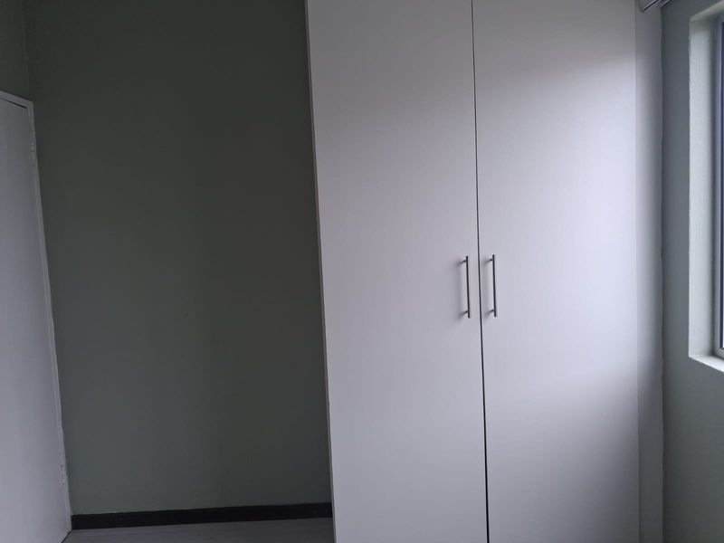 A clean, empty bedroom featuring a modern white built-in wardrobe and a window, providing a neutral space ready for personalization.