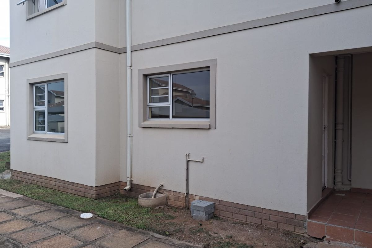 Exterior view of the apartment building featuring plastered walls, brick plinth, aluminium window frames, and a paved walkway.