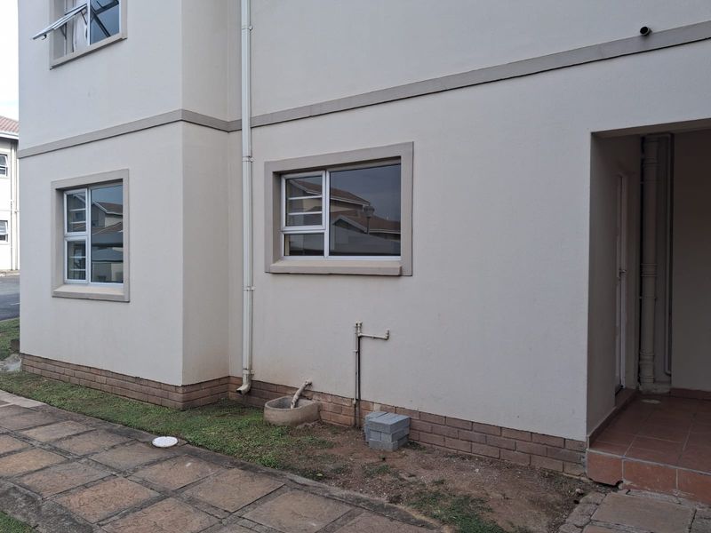 Exterior view of the apartment building featuring plastered walls, brick plinth, aluminium window frames, and a paved walkway.