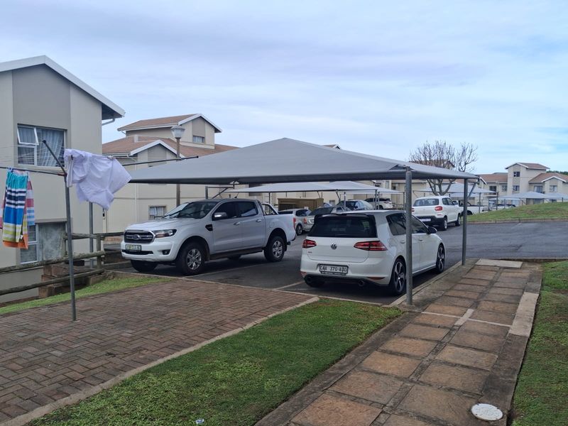 Exterior view of the apartment complex featuring a covered carport area with paved driveway and surrounding landscaped grounds.