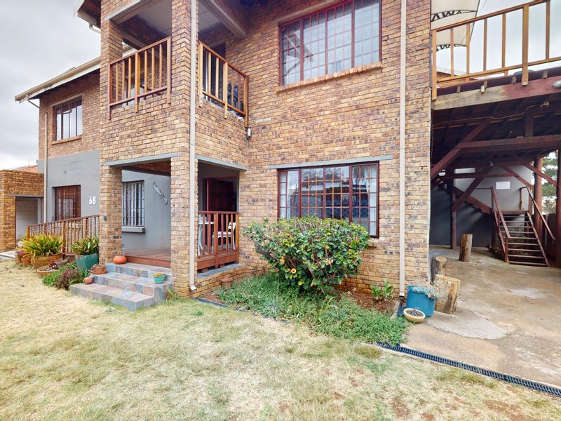 Front elevation of a multi-level face brick house featuring a covered entrance, timber balcony, and an external staircase leading to the upper level.