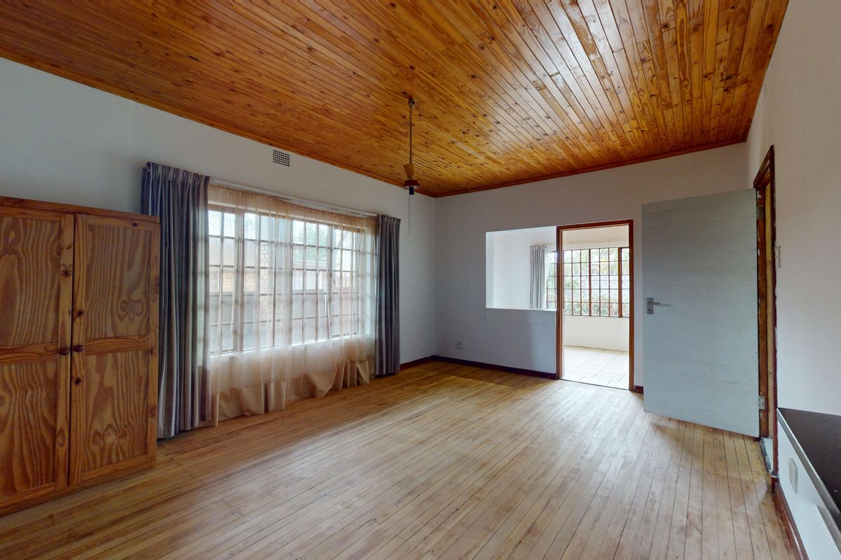 Spacious bedroom featuring warm timber ceiling and flooring, large window for natural light, and direct access to an adjoining room.