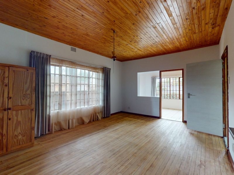 Spacious bedroom featuring warm timber ceiling and flooring, large window for natural light, and direct access to an adjoining room.