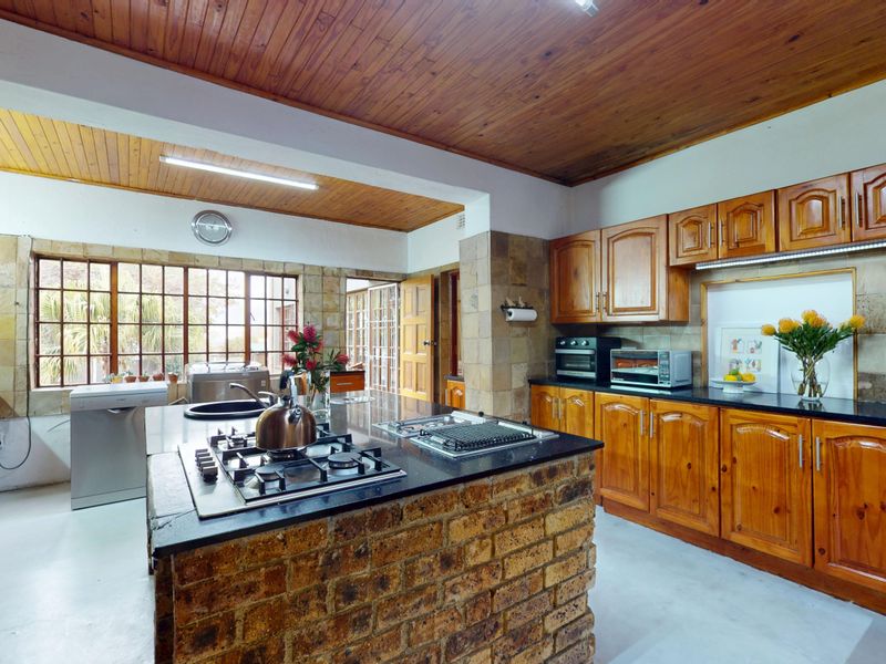 Spacious kitchen featuring a central brick island with gas hob, granite countertops, timber cabinetry, and a distinctive timber-clad ceiling.