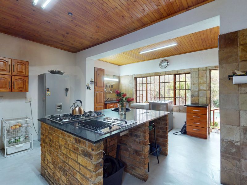 Spacious kitchen featuring a central brick island with granite countertops, built-in gas hob, grill, and rustic timber ceiling finishes.
