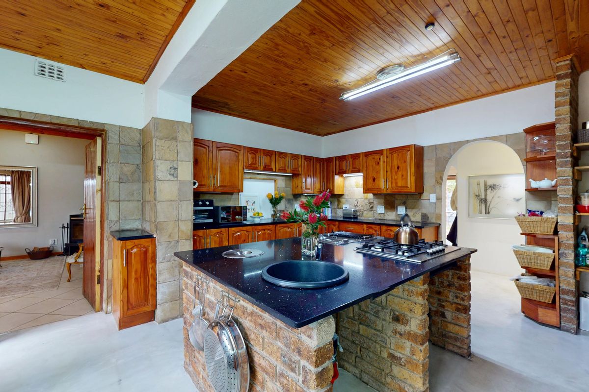 A rustic kitchen featuring a brick island with a stone countertop, built-in gas hob, timber cabinetry, and a distinctive timber-paneled ceiling.
