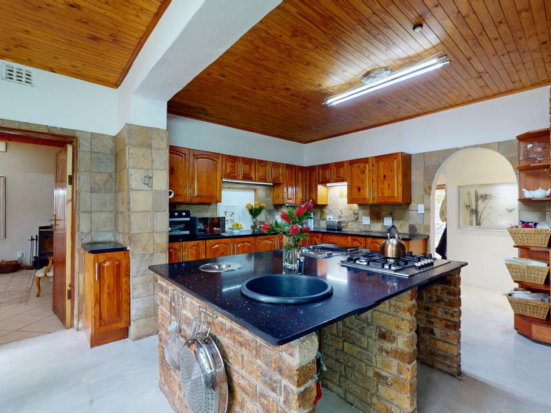 A rustic kitchen featuring a brick island with a stone countertop, built-in gas hob, timber cabinetry, and a distinctive timber-paneled ceiling.