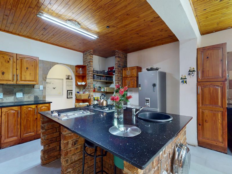 A rustic kitchen featuring wooden cabinetry, a brick-based island with a black granite countertop, stone tile backsplash, and a distinctive wooden ceiling.