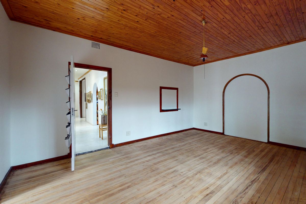 An empty living room featuring timber flooring and a timber-clad ceiling, with an arched wall opening leading to an adjacent hallway.