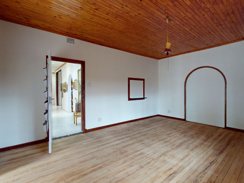 An empty living room featuring timber flooring and a timber-clad ceiling, with an arched wall opening leading to an adjacent hallway.
