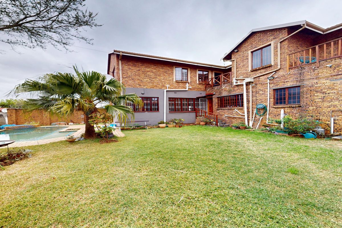 Rear view of a double-story brick house featuring a swimming pool, lawn area, and a timber balcony.