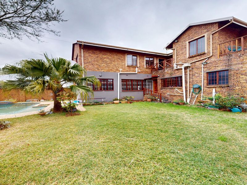 Rear view of a double-story brick house featuring a swimming pool, lawn area, and a timber balcony.