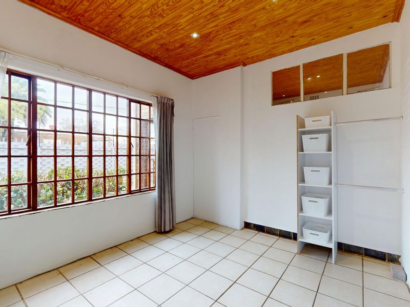 A bright, empty bedroom featuring a natural timber ceiling, tiled flooring, and a large window providing ample natural light.