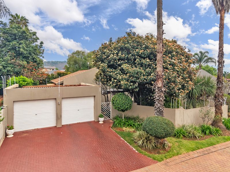 Front view of the townhouse featuring a double garage, paved driveway, and established garden with perimeter wall and electric fencing.