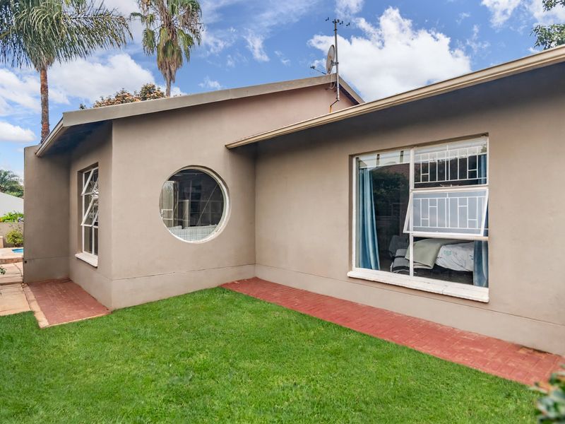 Rear exterior view of the townhouse featuring a lawn, brick pathways, and a distinctive circular window with security bars.