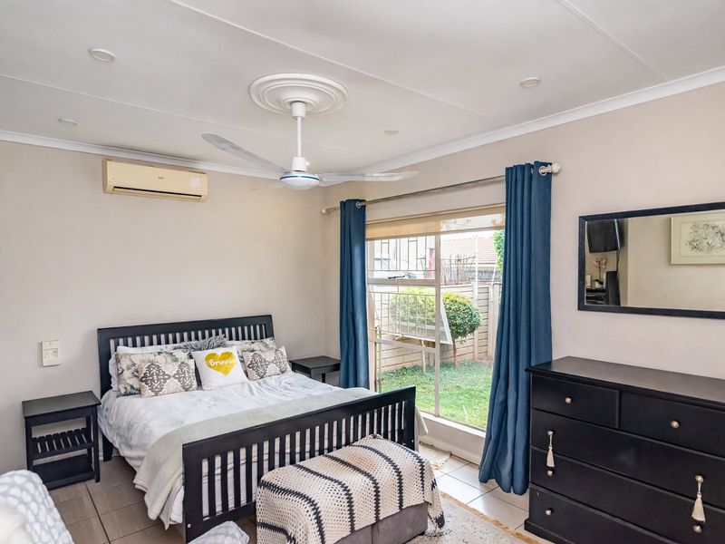 A well-lit bedroom featuring tiled flooring, a ceiling fan, and a wall-mounted air conditioning unit, with direct access to a small garden area.