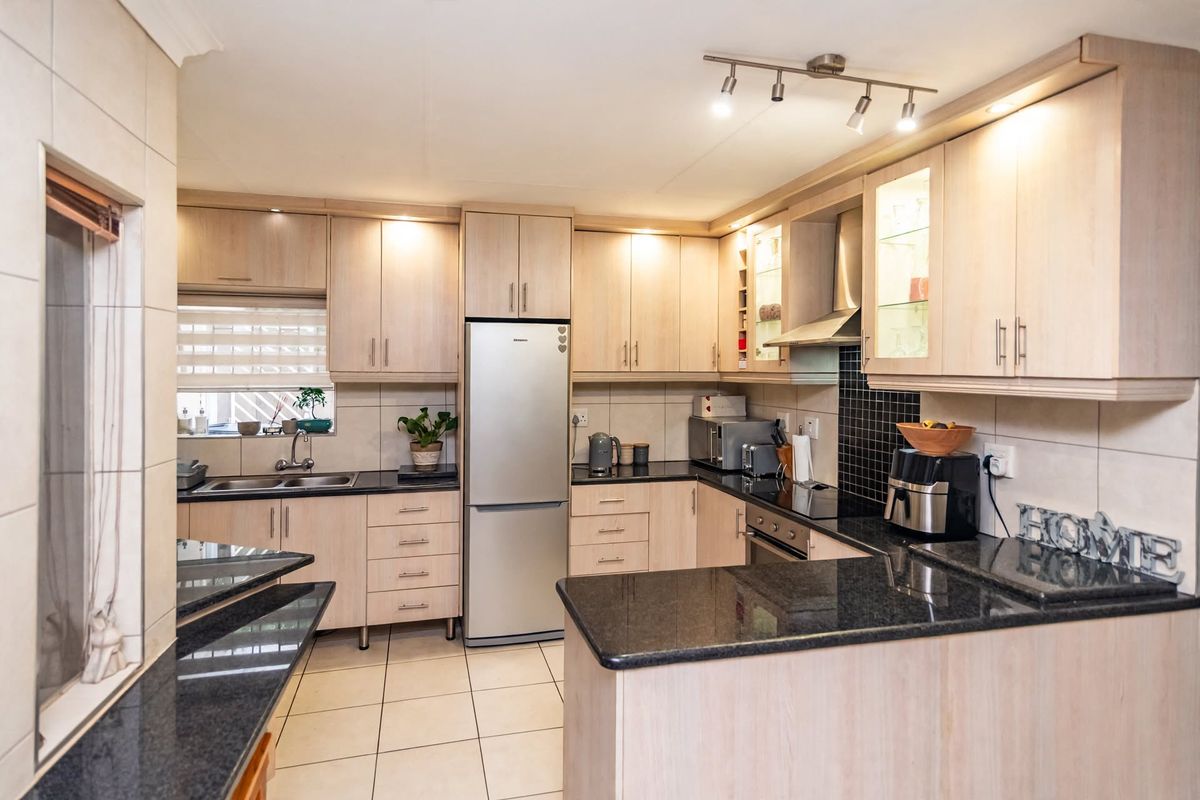 A functional kitchen featuring light wood cabinetry, dark granite countertops, tiled backsplash, and integrated appliances, offering a clean and well-maintained workspace.