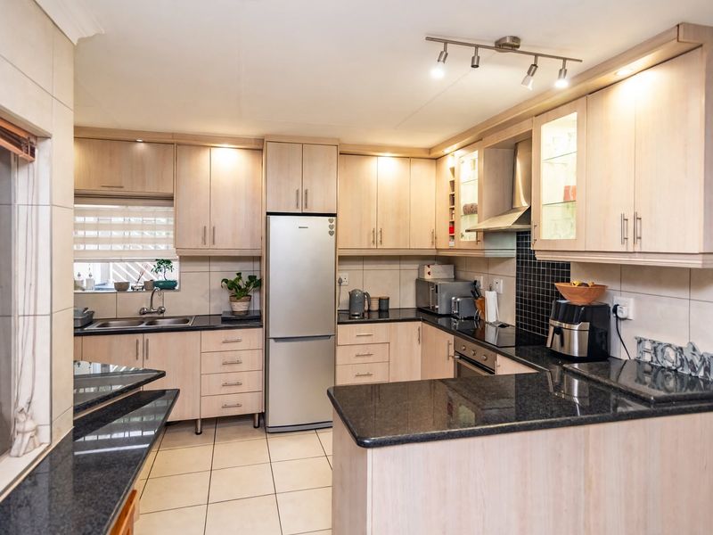 A functional kitchen featuring light wood cabinetry, dark granite countertops, tiled backsplash, and integrated appliances, offering a clean and well-maintained workspace.