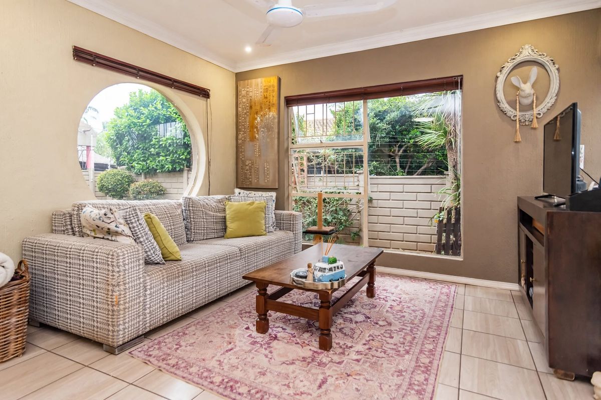 A cozy living room featuring unique circular and rectangular windows, tiled flooring, and a ceiling fan, offering a bright and comfortable living space.