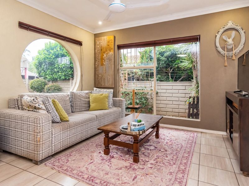 A cozy living room featuring unique circular and rectangular windows, tiled flooring, and a ceiling fan, offering a bright and comfortable living space.