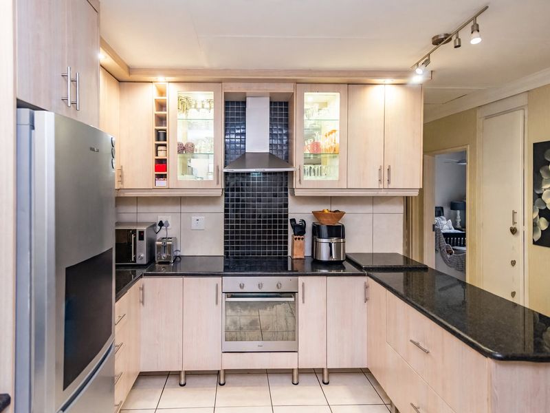 A well-maintained kitchen featuring light wood cabinetry, granite countertops, a tiled backsplash, and integrated stainless steel appliances with modern track lighting.