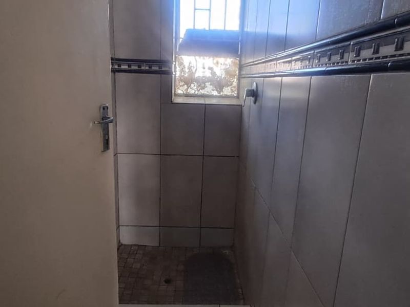 A compact shower area featuring tiled walls and flooring, equipped with a window for natural light and ventilation.