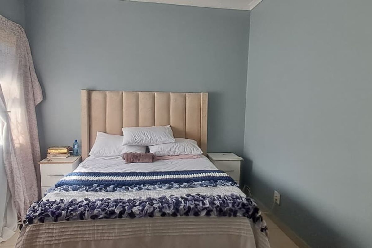 A bedroom featuring blue painted walls, a window with a security gate, and neutral flooring.