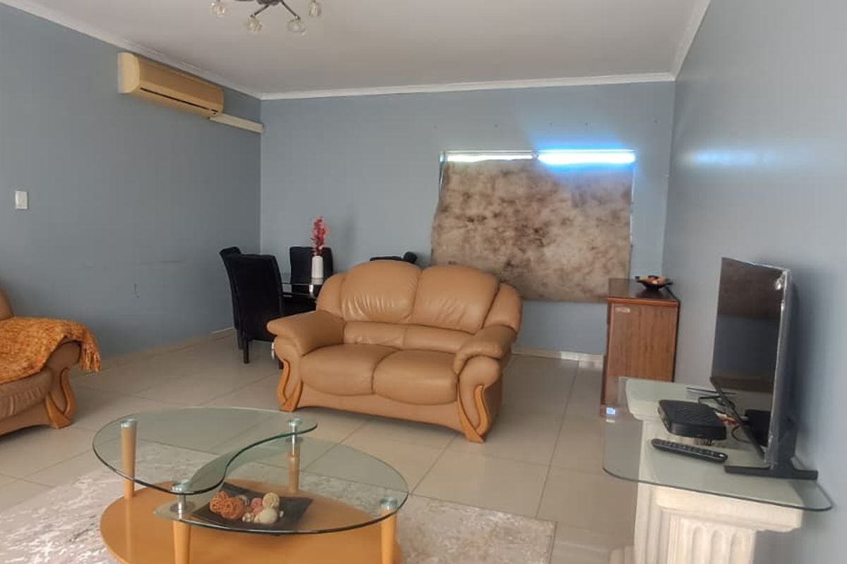 A spacious living room featuring tiled flooring, coving, and a wall-mounted split-system air conditioner.